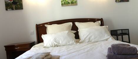 A neatly made bed with white linens and multiple pillows, a wooden headboard, and two wall-mounted light fixtures.