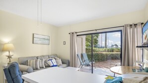 A hotel room with a sofa, a dining table, a chair, a lamp, and a view of the outdoors. - Escape to the beach! (Destin)