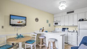 A compact kitchen with a dining area, a TV mounted on the wall, and a ceiling fan. - Escape to the beach! (Destin)