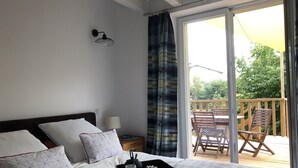 Ein Schlafzimmer mit Bett, Kissen, einem Tablett mit Tassen und Teekanne, einem Nachttisch, einer Lampe und Blick auf eine Terrasse mit Stühlen.