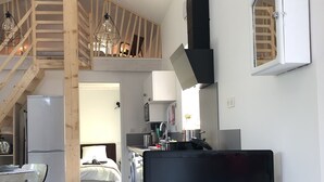 Een moderne woonruimte met een flatscreen televisie op een houten standaard, een keukenhoek met een wasmachine, en een trap die naar een hoger niveau leidt.