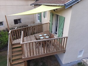 A wooden deck with a table set for four, a yellow canopy, and a stone wall.