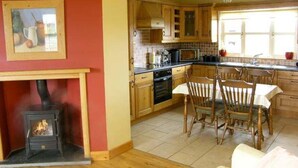 A cozy kitchen with wooden cabinets, a dining area with a table and chairs, and a fireplace. - Scenic Estuary Way 3-bed Home in Labasheeda (Labasheeda)