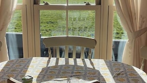 A dining area with a table and chairs, a view of a body of water, and curtains. - Scenic Estuary Way 3-bed Home in Labasheeda (Labasheeda)