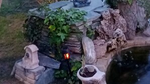 A garden statue of a seated figure with a light, surrounded by greenery and a small pond. - "A CUSTOM NEST by the sea! " (Lucciana)