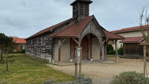 A rustic wooden building with a steeply pitched roof and a prominent chimney, likely a historical or cultural site.