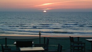 A seaside view with a sunset, a table, and chairs on a terrace.