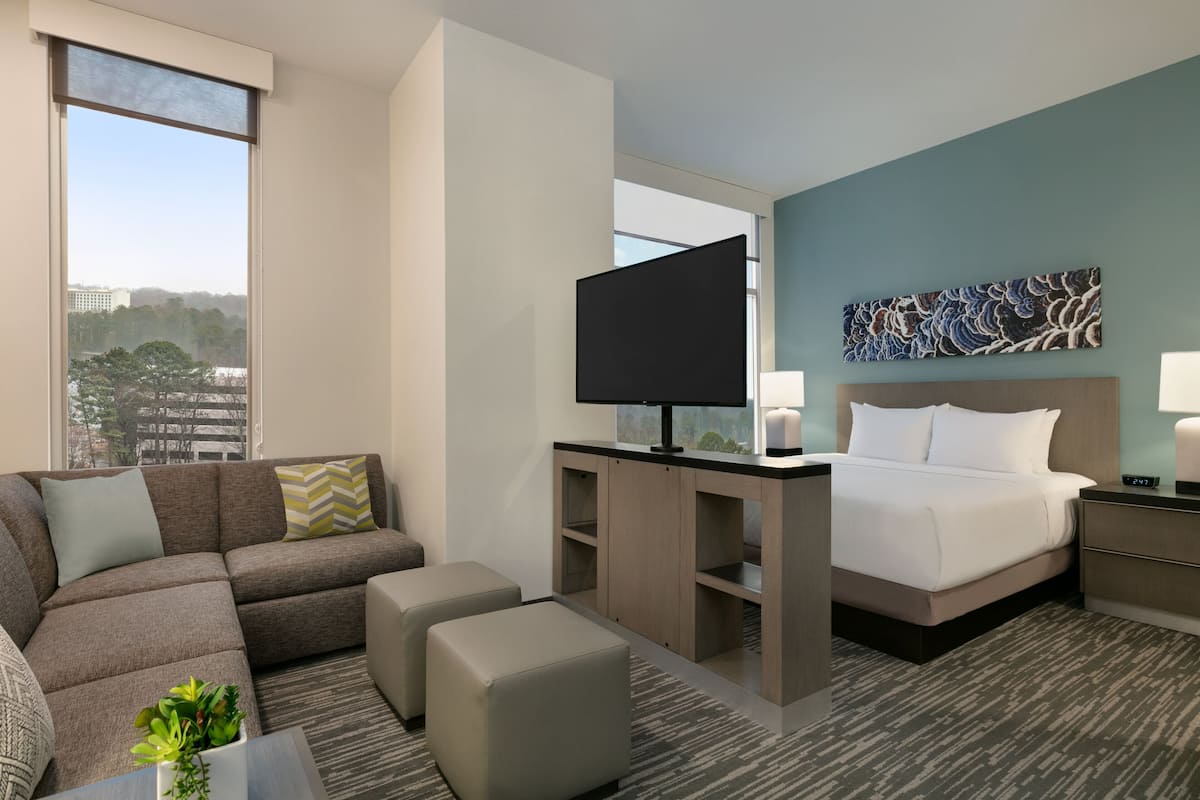 A modern hotel room with a large bed, a sofa, a TV, and a desk.