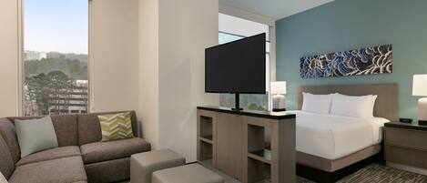A modern hotel room with a large bed, a sofa, a TV, and a desk.