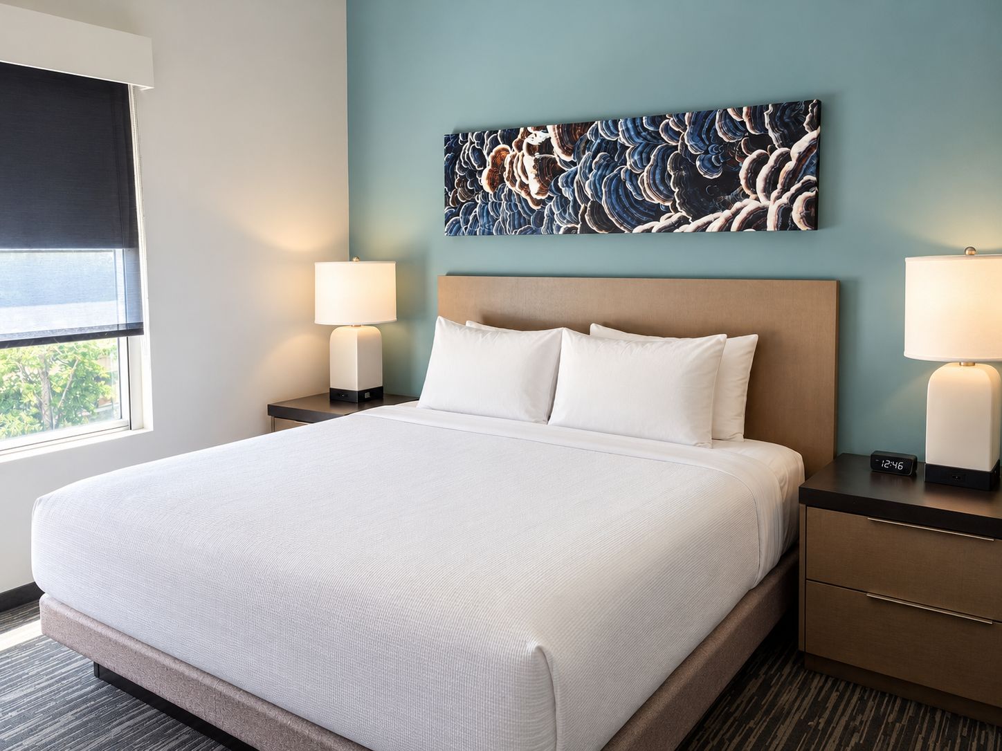 A hotel room with a large bed, two bedside tables, a wall-mounted artwork, and a window with a view.