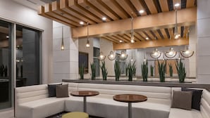 A modern lobby with a sectional sofa, two round tables, and hanging pendant lights. - Hyatt House Atlanta / Perimeter Center (Atlanta)