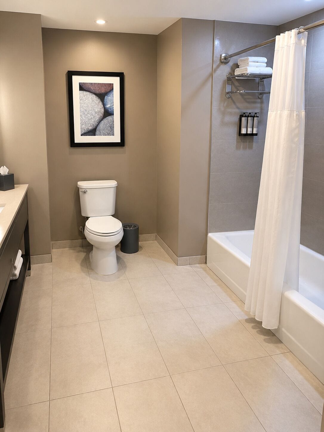 A modern bathroom with a toilet, a framed picture on the wall, a shower area with a curtain, and a sink with a towel rack.