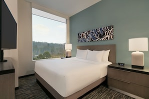 Relax in a spacious room with a large bed and forest views, featuring a flat-screen TV and two bedside tables with lamps.