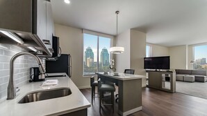 A modern kitchen with a large island, a dining area with bar stools, a flat-screen TV, and a city view through large windows. - Hyatt House Atlanta / Perimeter Center (Atlanta)
