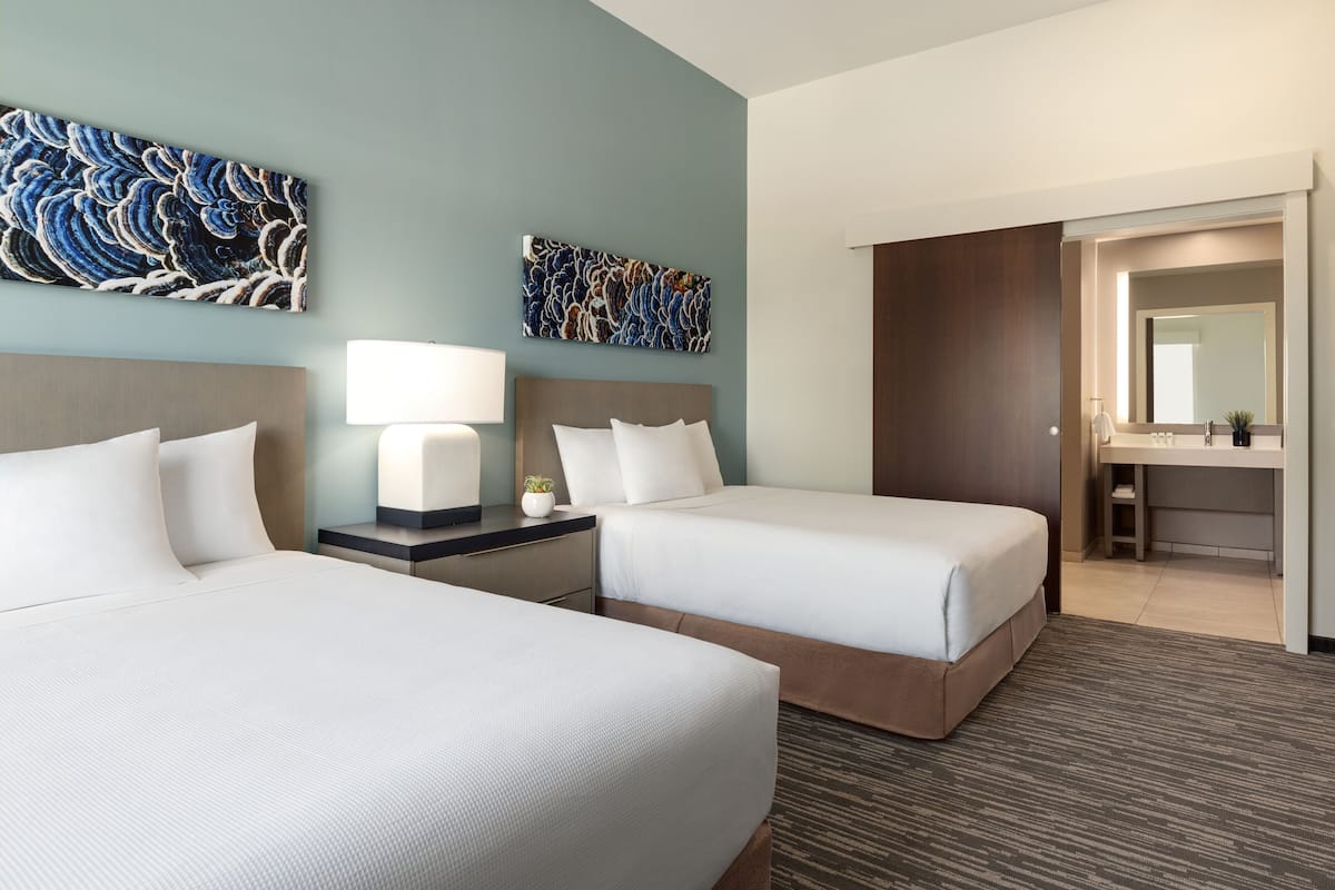 A hotel room with two beds, a desk, a mirror, and artwork on the walls.