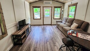 Ein gemütliches Zimmer mit Holzboden, einer Couch, einem Fernseher und einem Tisch mit Unterlage.