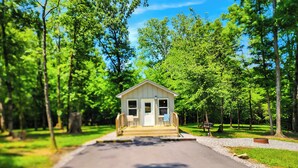Eine kleine, eingeschossige Holzhütte mit Veranda, umgeben von einem bewaldeten Gebiet.