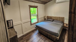 Ein Schlafzimmer mit Holzboden, einem Fenster mit Blick auf Grünflächen, einem Bett mit Holz-Kopfteil und einer Klimaanlage.