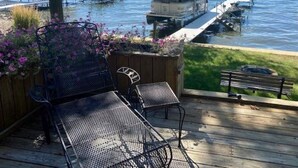 A wooden deck with metal chairs and a table overlooking a lake with boats.