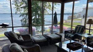 A spacious room with large windows offering a view of a lake and a statue. There are wicker furniture pieces, including a sofa and chairs, and a small table with a tray.
