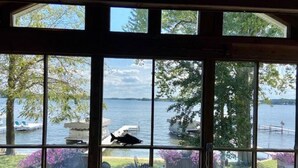 A room with large windows overlooking a lake, a chair, and a grill.