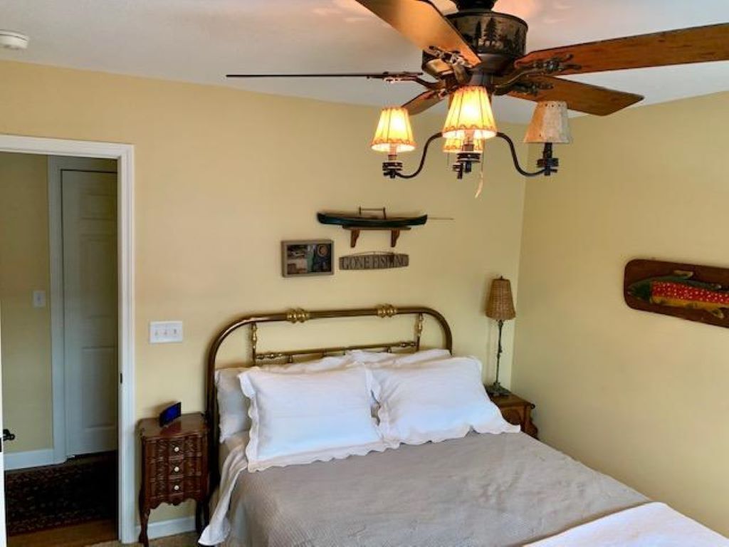 A bedroom with a bed, a ceiling fan, a nightstand, and a wall-mounted lamp.