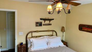 A bedroom with a bed, a ceiling fan, a nightstand, and a wall-mounted lamp.