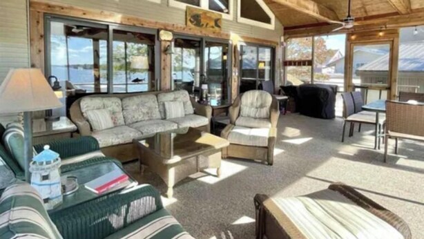A cozy interior with a sofa, armchairs, and a dining area, featuring large windows and wooden beams.