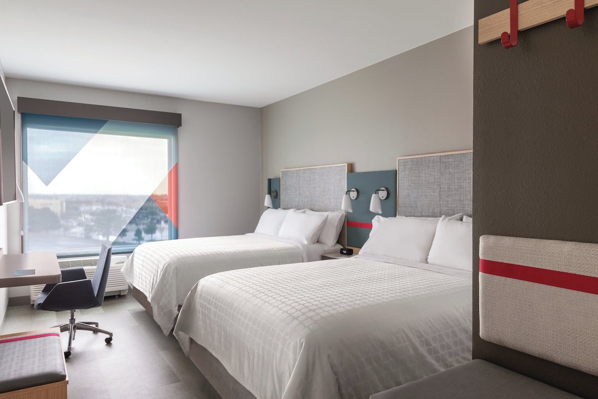 A hotel room with two beds, a desk, and a chair.