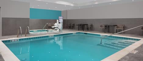 Une piscine intérieure à l’eau d’un bleu limpide, dotée d’un plongeoir et d’un espace détente avec des chaises et des tables.