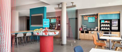 Een modern café met een centrale fruitvitrine, een zitgedeelte en een koffiemachine.