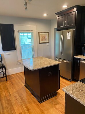 A kitchen with a central island, dark cabinetry, stainless steel appliances, and a window with blinds.