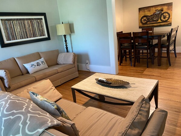 A living room with a sofa, a coffee table, and a dining area with chairs and a table.
