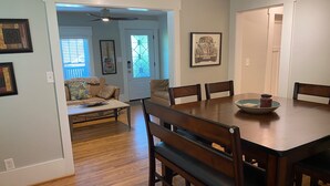 Un comedor con mesa de madera, sillas y un cuenco decorativo. Se observa una puerta con un vitral y un ventilador de techo.