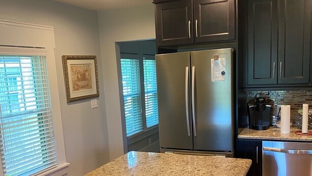 Una cocina con armarios oscuros, un refrigerador de acero inoxidable, un lavavajillas y una isla con encimera de granito.