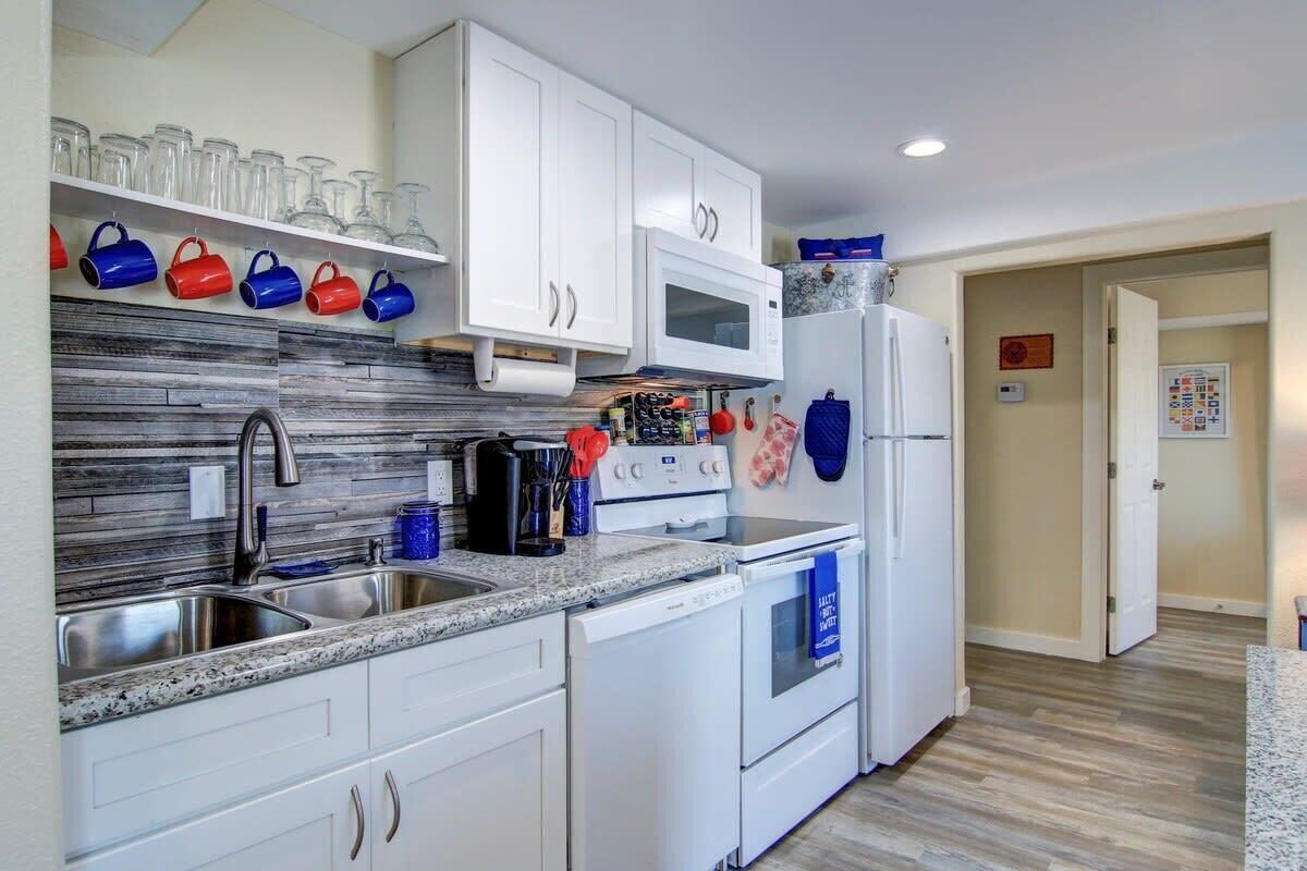 Una cocina moderna con gabinetes blancos, una encimera de granito, un microondas y un refrigerador.