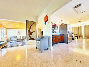 Um hall amplo com piso lustroso, uma grande escultura, uma área de estar e uma cozinha com geladeira e prateleiras.