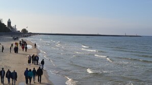 A beach with people walking along the shore, a lighthouse in the background, and a pier extending into the water. - Apartment Kolberg 10 Minutes Walk From the Beach (Kolobrzeg)
