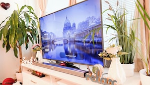 Ein Fernseher auf einer weißen Unterhaltungsecke mit einem Schild mit der Aufschrift 'Relax', einem Fußball und einer Pflanze.