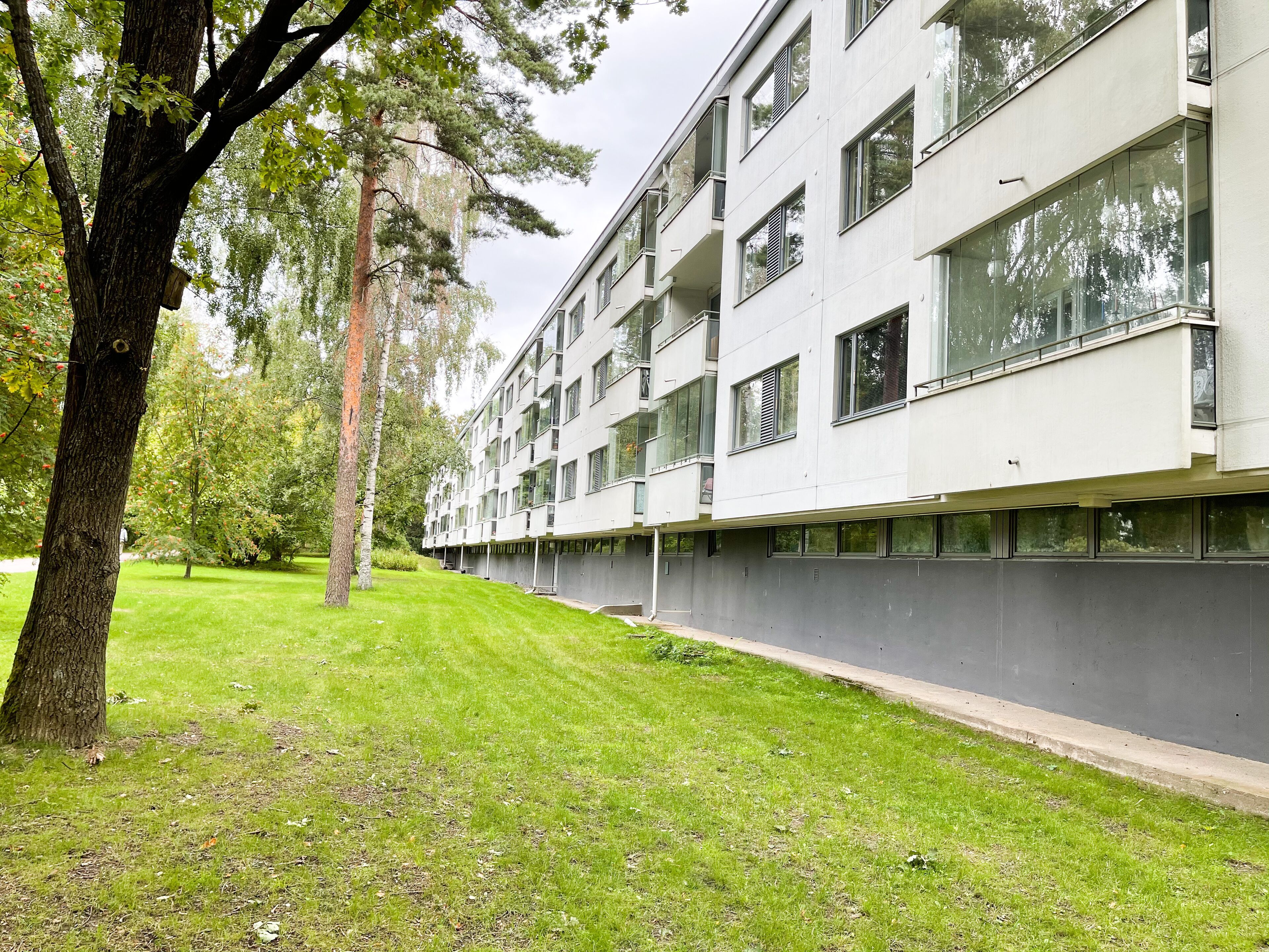 Un edificio moderno de varios pisos con grandes ventanales y balcones, rodeado de un césped cuidado y árboles.