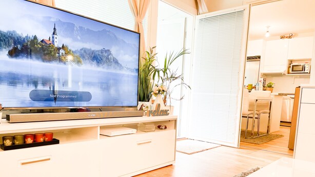 Ein modernes Wohnzimmer mit Flachbildfernseher auf einer weißen Unterhaltungseinheit, einem Essbereich mit weißem Tisch und einer Küchenzeile inklusive Mikrowelle.
