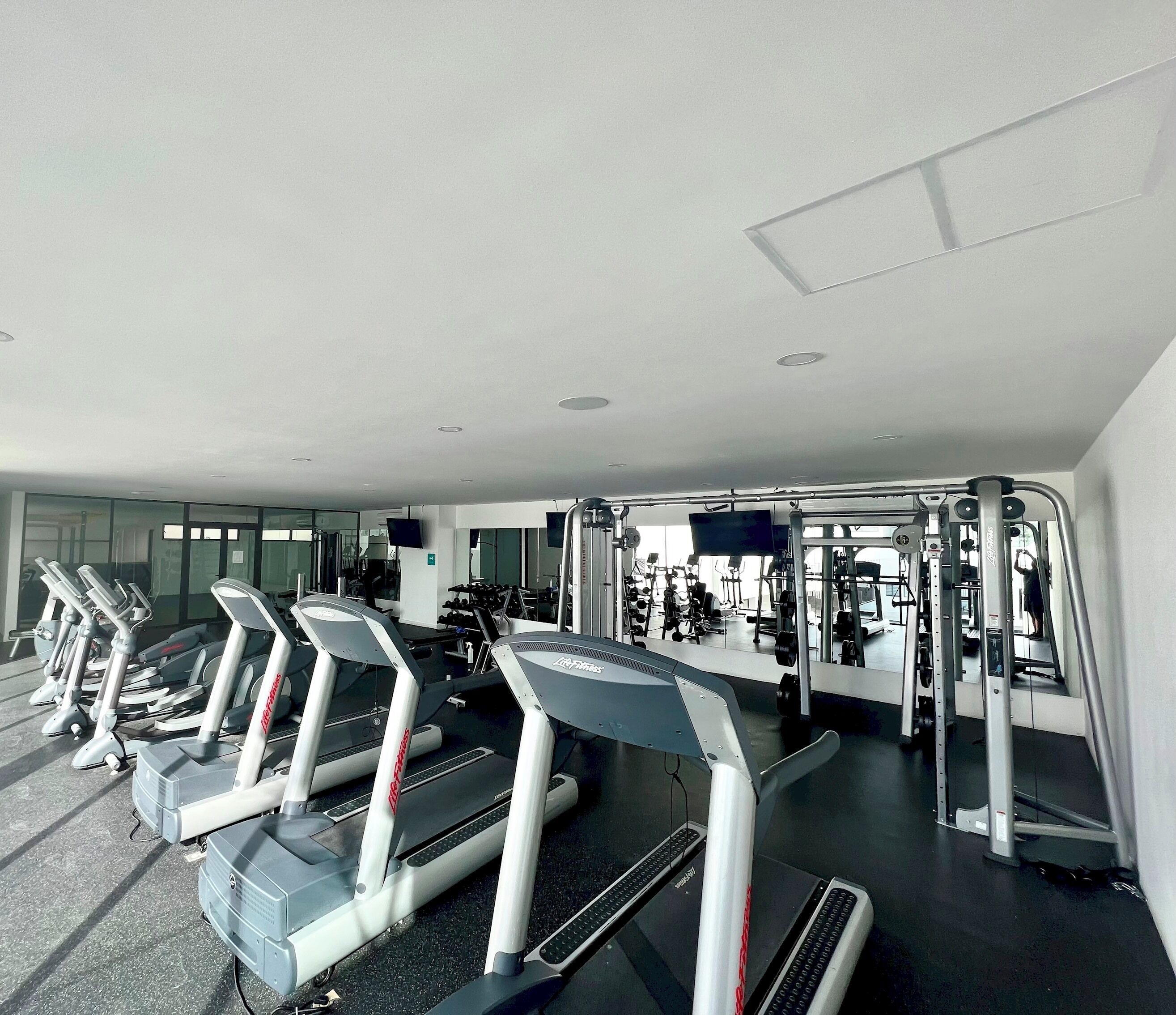Un gimnasio con cintas de correr, máquinas de pesas y un espejo grande.
