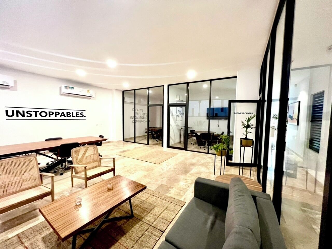 Espaço de escritório moderno com uma grande mesa de reunião, área de estar e paredes de vidro.