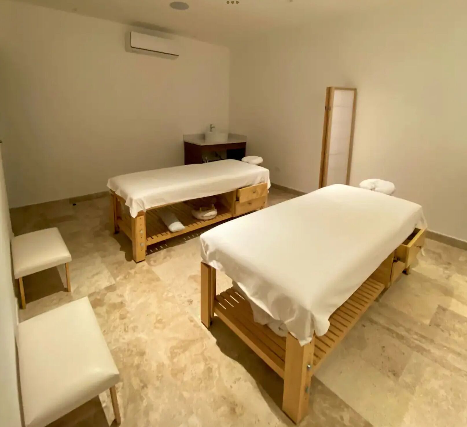 Una habitación con dos camas de madera, un pequeño banco, un espejo y un lavamanos.