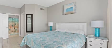 A bedroom with a bed, nightstands, a ceiling fan, a door leading to another room, and a painting on the wall.