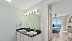 Un baño con dos lavamanos, un espejo grande con iluminación y vistas a un balcón con cama.