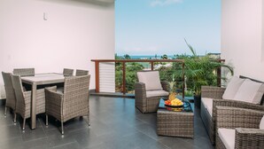 A balcony with wicker furniture, a dining table, and a view of the ocean.