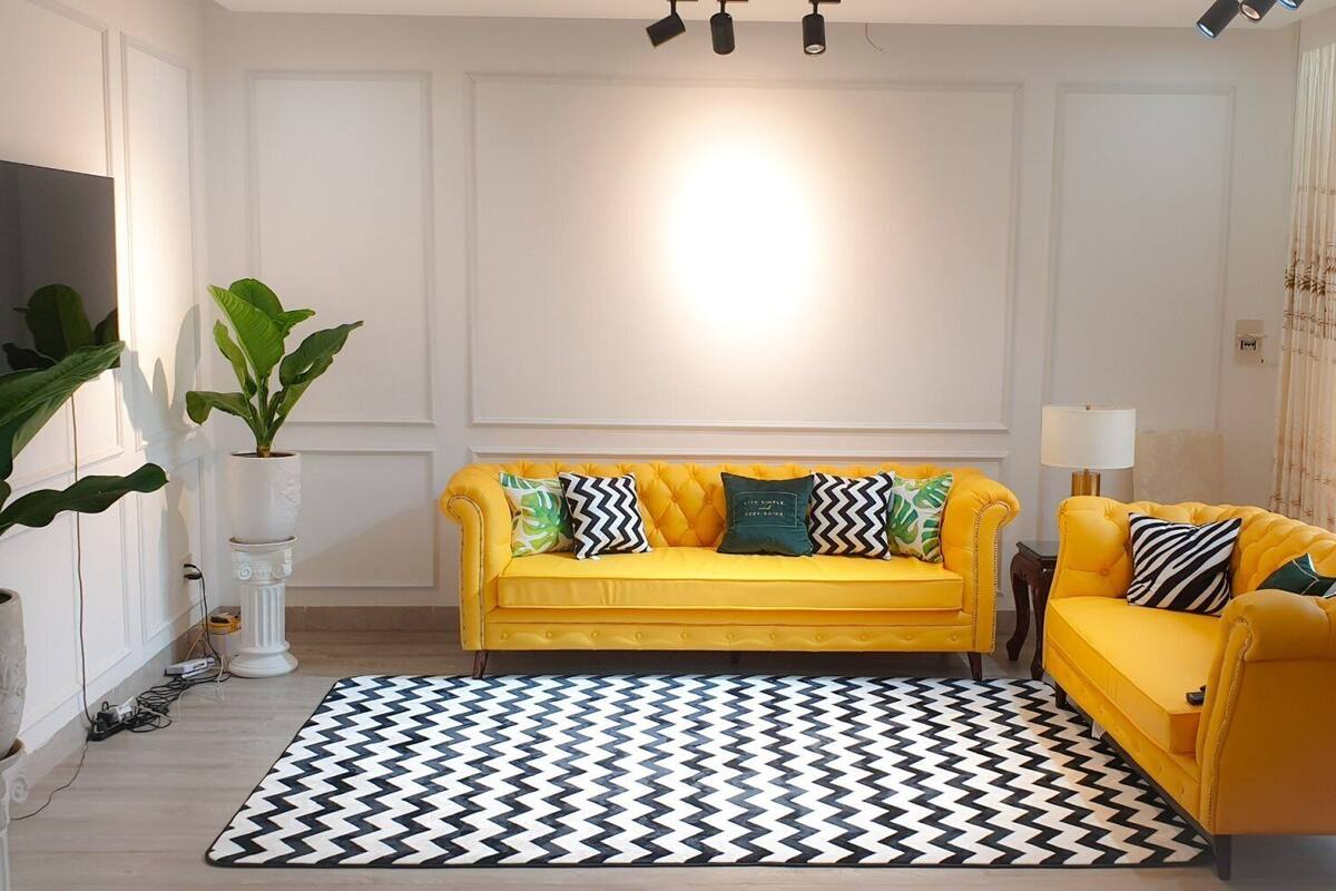 A living room with a yellow sofa, a patterned rug, and a large window with a view.
