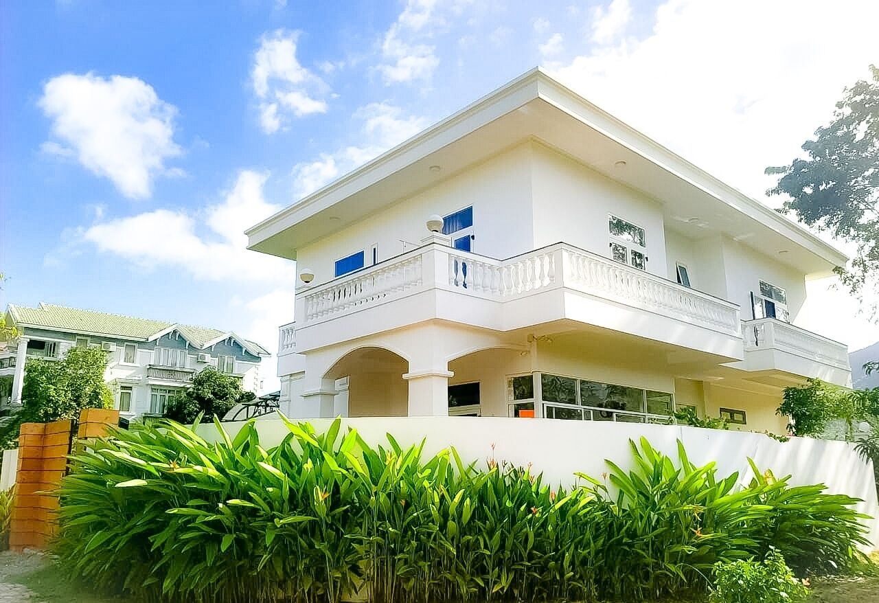 A two-story building with a balcony, surrounded by lush greenery.
