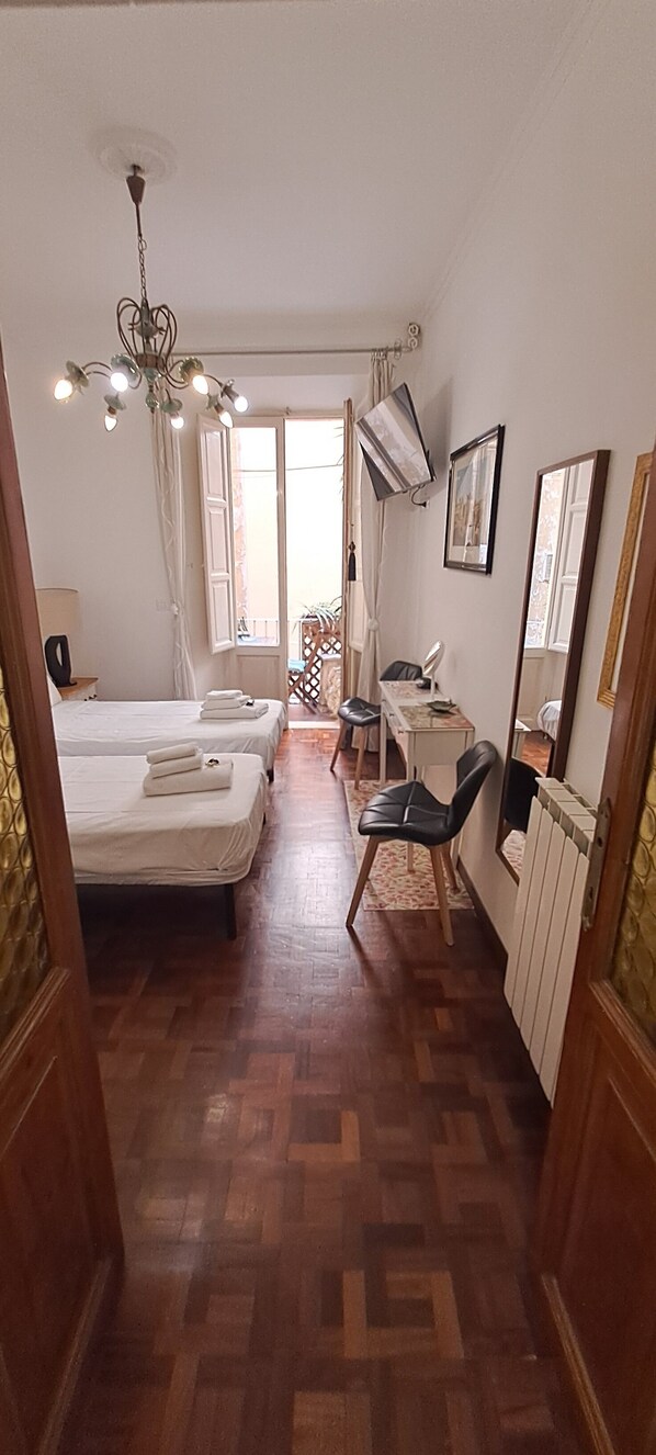 A hotel room with two beds, a desk, a chair, a radiator, and a mirror.